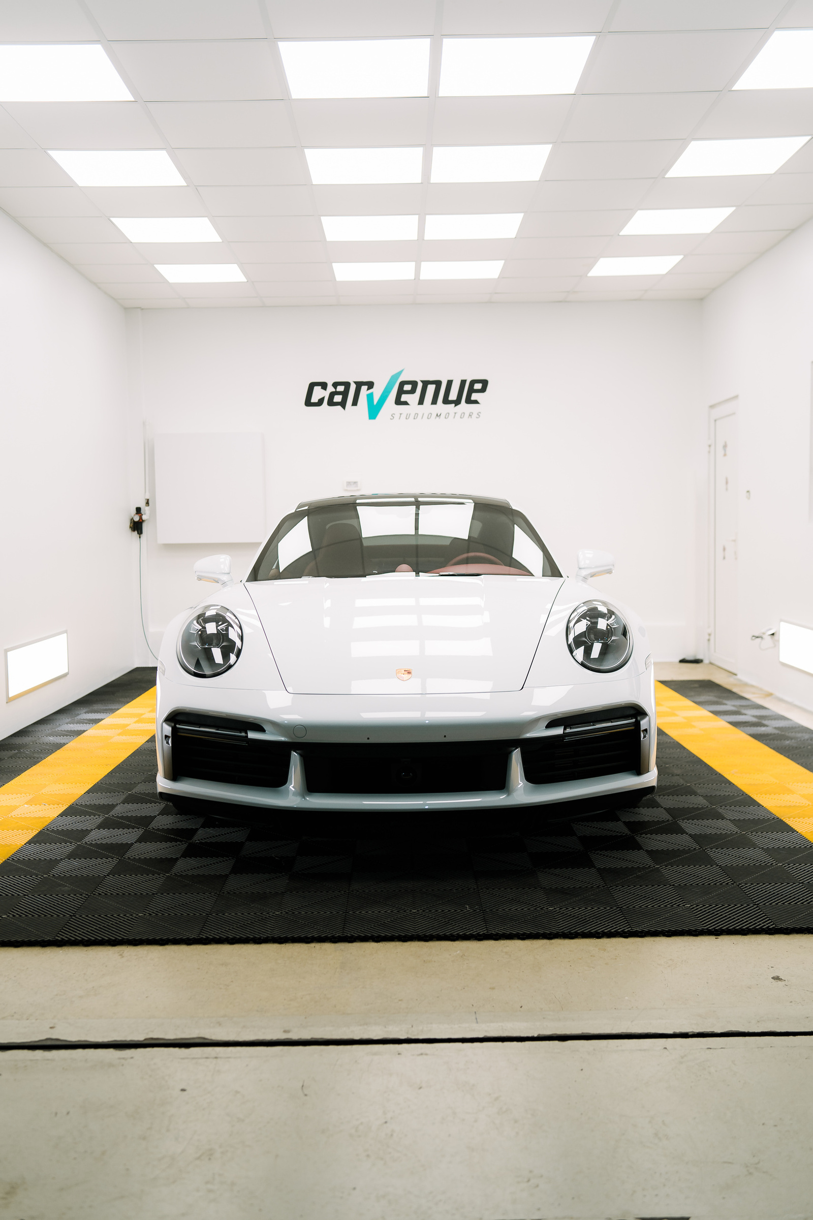 Light grey Porsche 911 Turbo S seen head-on in the CarVenue studio, under the lit ceiling