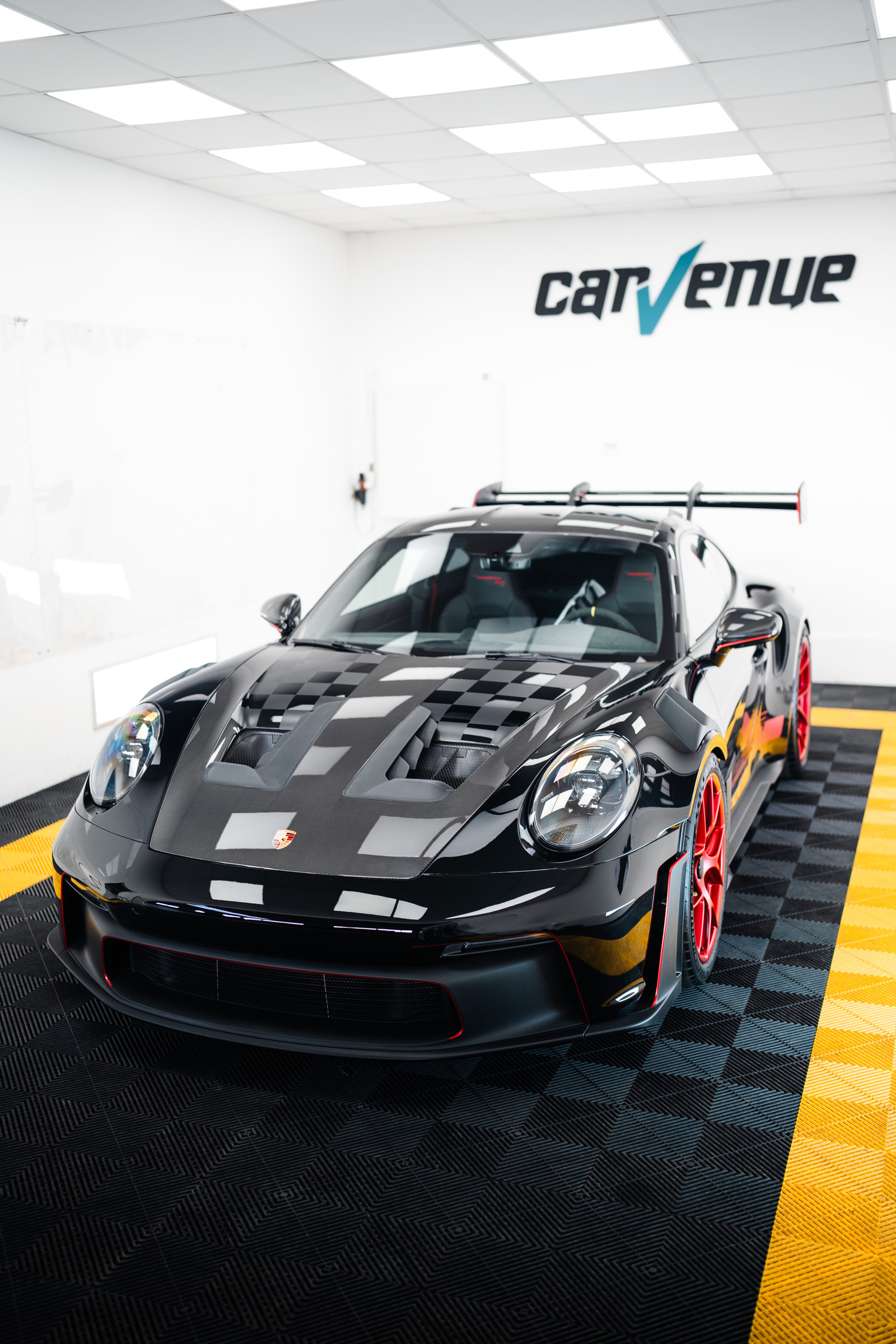 Black Porsche 911 GT3 RS with red wheels and a chequered bonnet, parked in the CarVenue studio