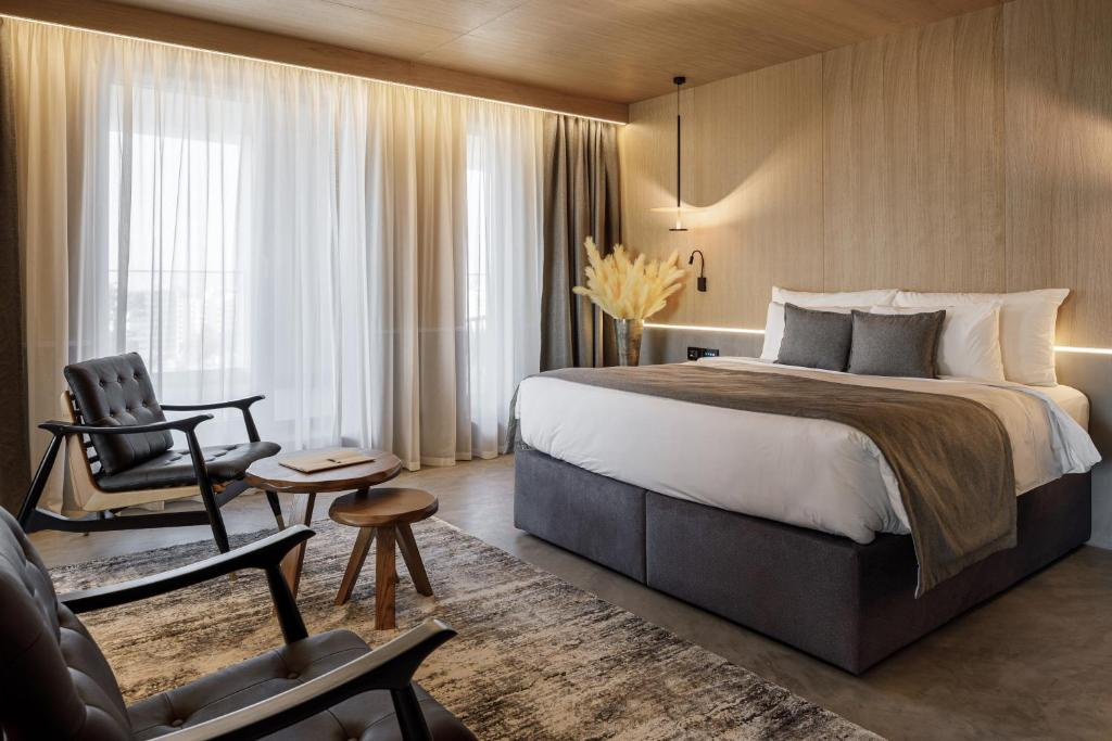 Room at Hotel Qosmo Brașov with a double bed, wood panelling and two black tufted armchairs by the window