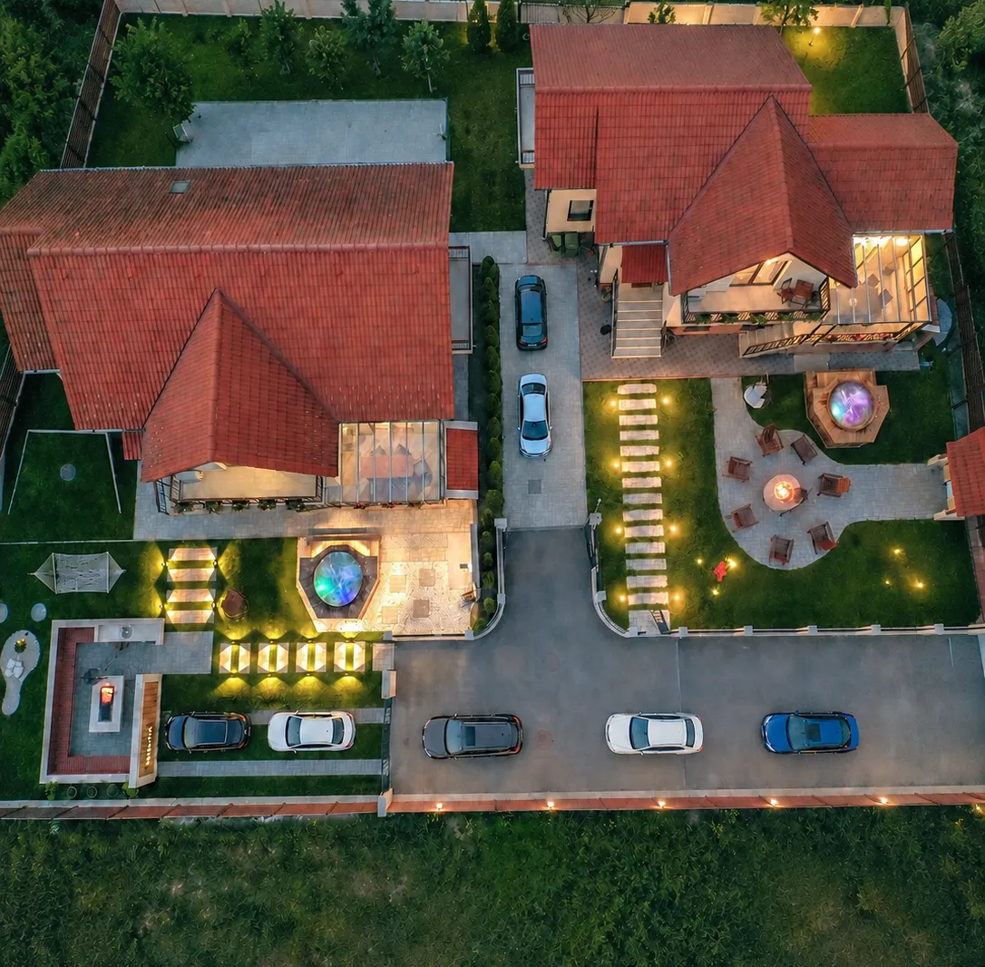 ROOTS Villas from above at dusk: red-roofed houses, lit hot tubs, a fire pit with chairs and cars parked out front