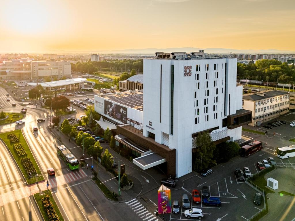 The white Hotel Kronwell Brașov building seen from above in golden light, with the boulevard and car park around it