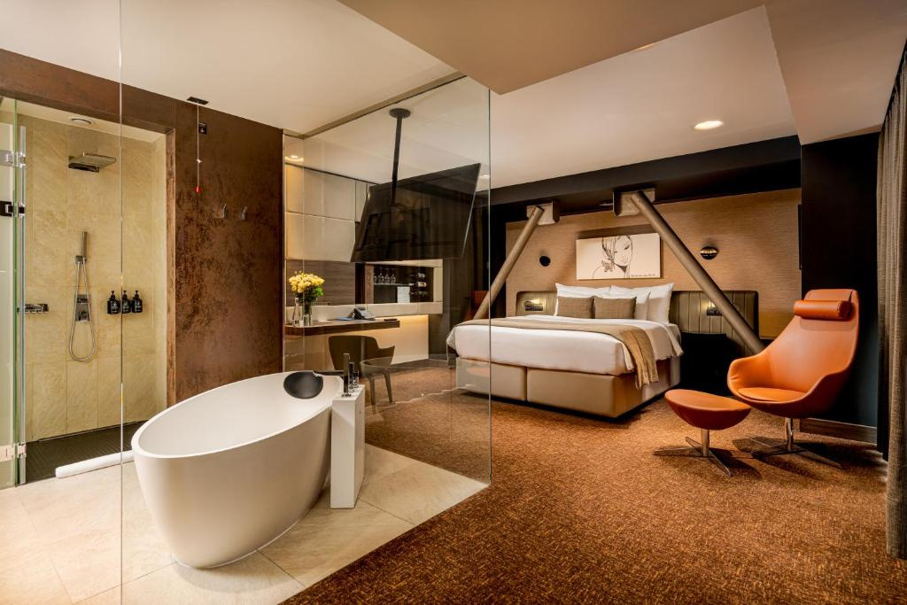 Room at Hotel Kronwell Brașov with a freestanding bathtub, glass-walled shower, double bed and an orange armchair