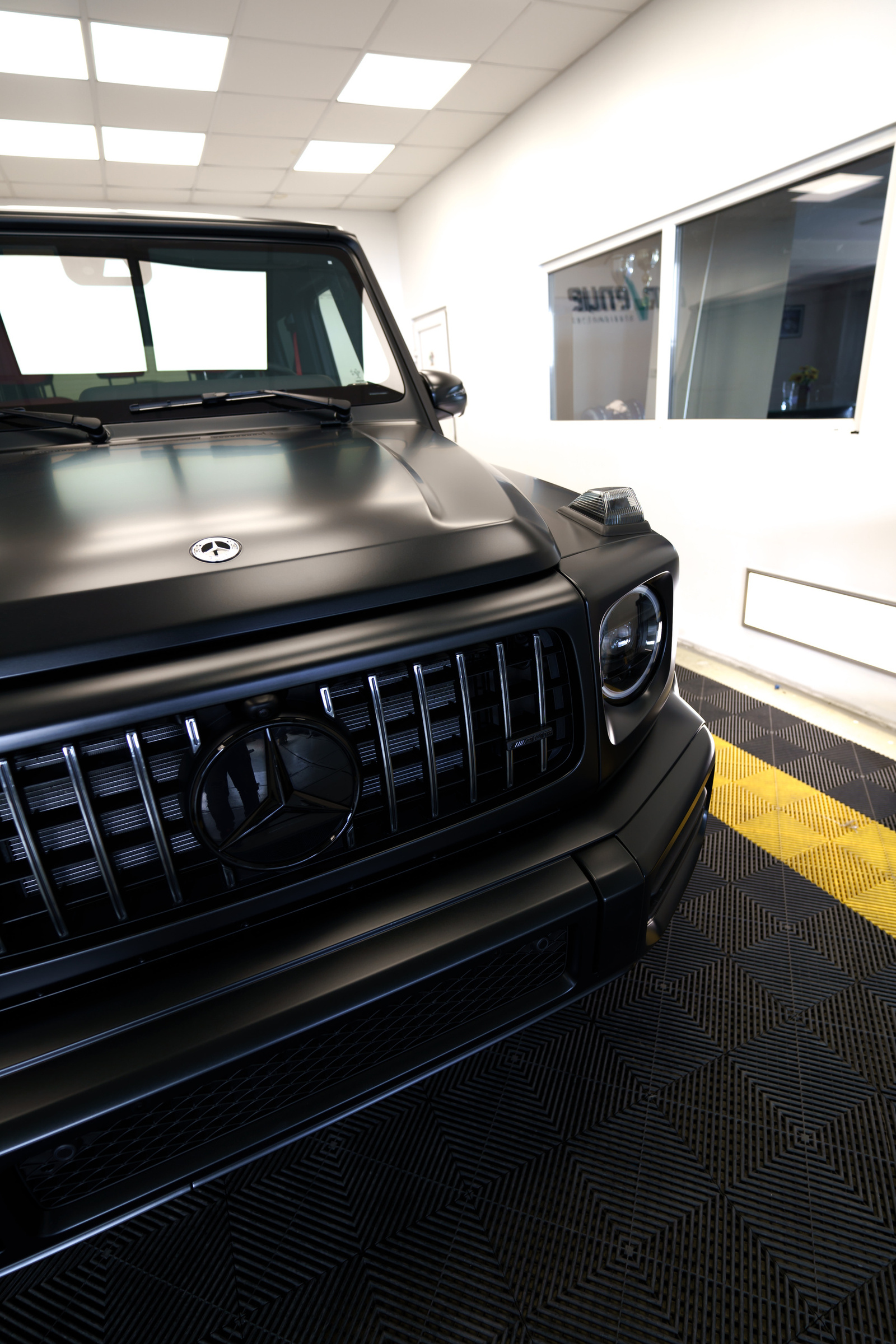 Front end of a matte black Mercedes-AMG G-Class in the studio: the grille with vertical chrome bars and a round headlight